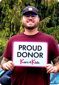 A person holding a sign that says Proud Donor Kars4Kids
