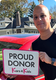 A person holding a sign that says Proud Donor Kars4Kids