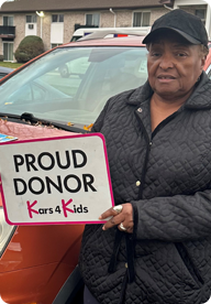 A person holding a sign that says Proud Donor Kars4Kids