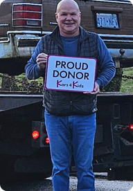 A person holding a sign that says Proud Donor Kars4Kids